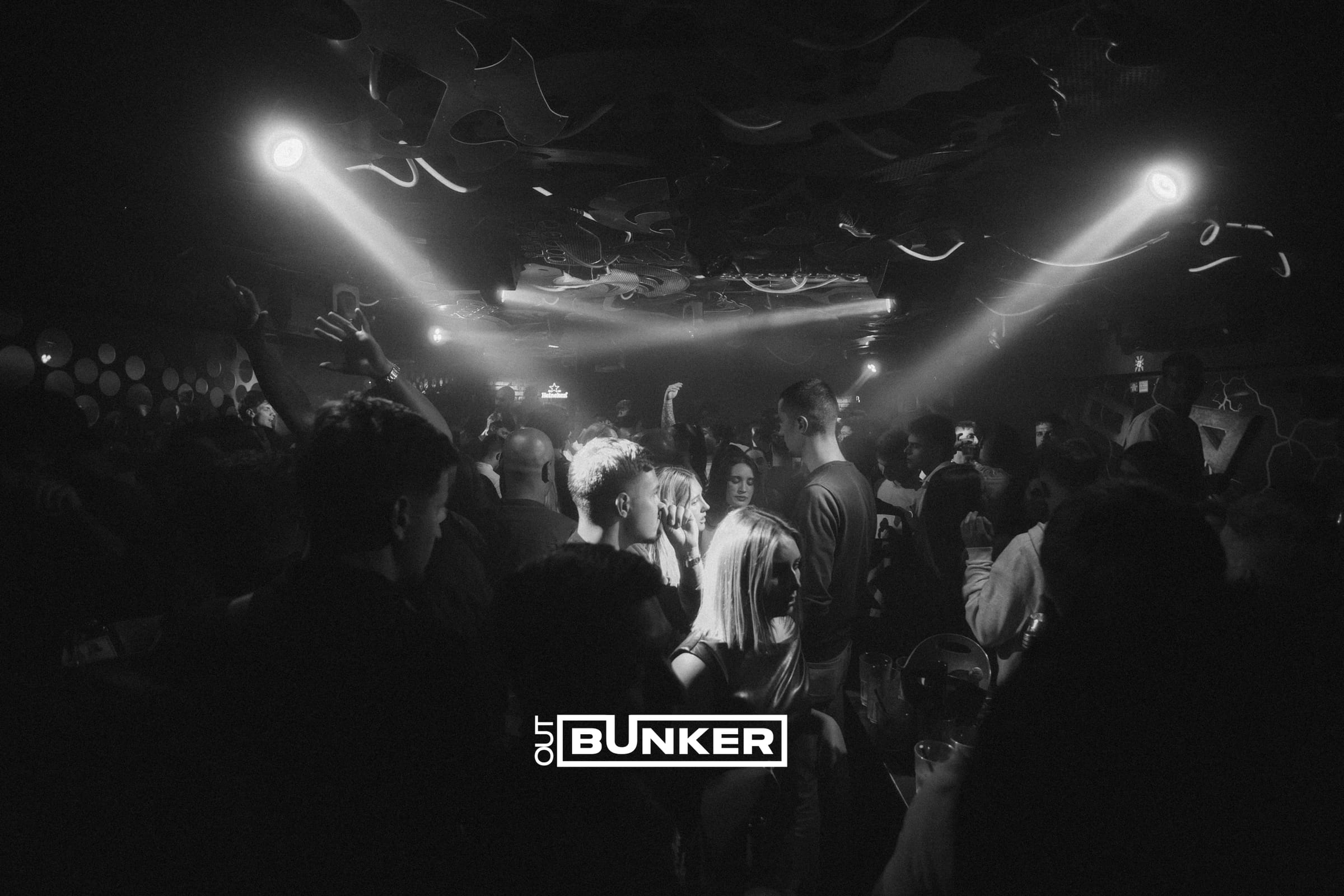 Crno-bijela fotografija publike koja pleše pod reflektorima na partyju Out Bunker